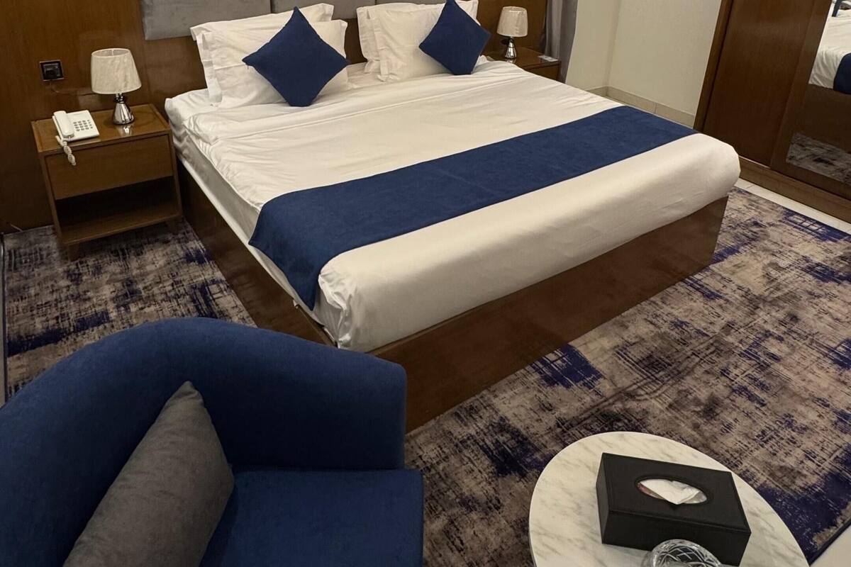 Une chambre d’hôtel avec un grand lit, une table de chevet avec une lampe, une chaise et une petite table ronde sur laquelle se trouve une boîte de mouchoirs.