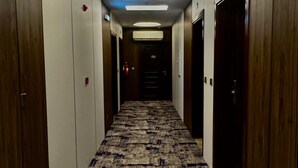 A hotel hallway with a patterned carpet, wooden doors, and a neon exit sign. - Hayat Al Aseel Hotel Apartments (Jeddah)