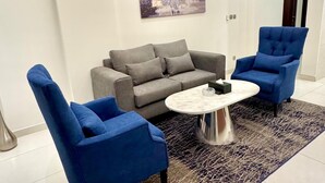 A modern living room with a grey sofa, two blue armchairs, a marble coffee table, and a patterned rug. - Hayat Al Aseel Hotel Apartments (Jeddah)
