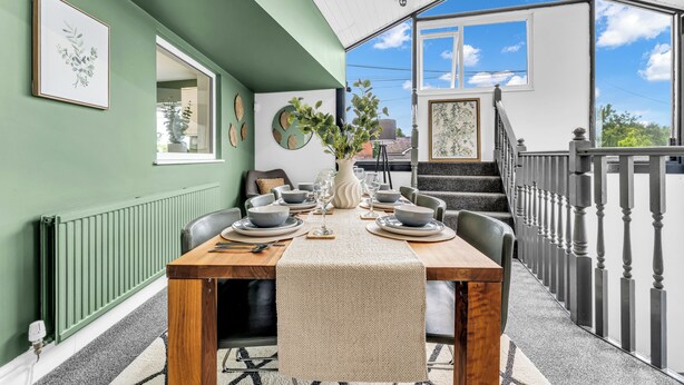 A dining area with a table set for four, a staircase, and a view of the sky.