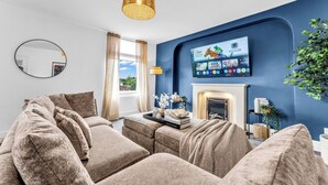 A modern living room with a blue accent wall, a flat-screen TV, a fireplace, and a large window with curtains.
