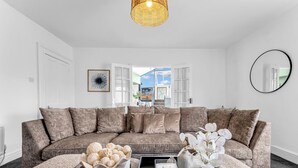 A modern living room with a sectional sofa, a coffee table with decorative items, a large mirror, and a view through an open door.