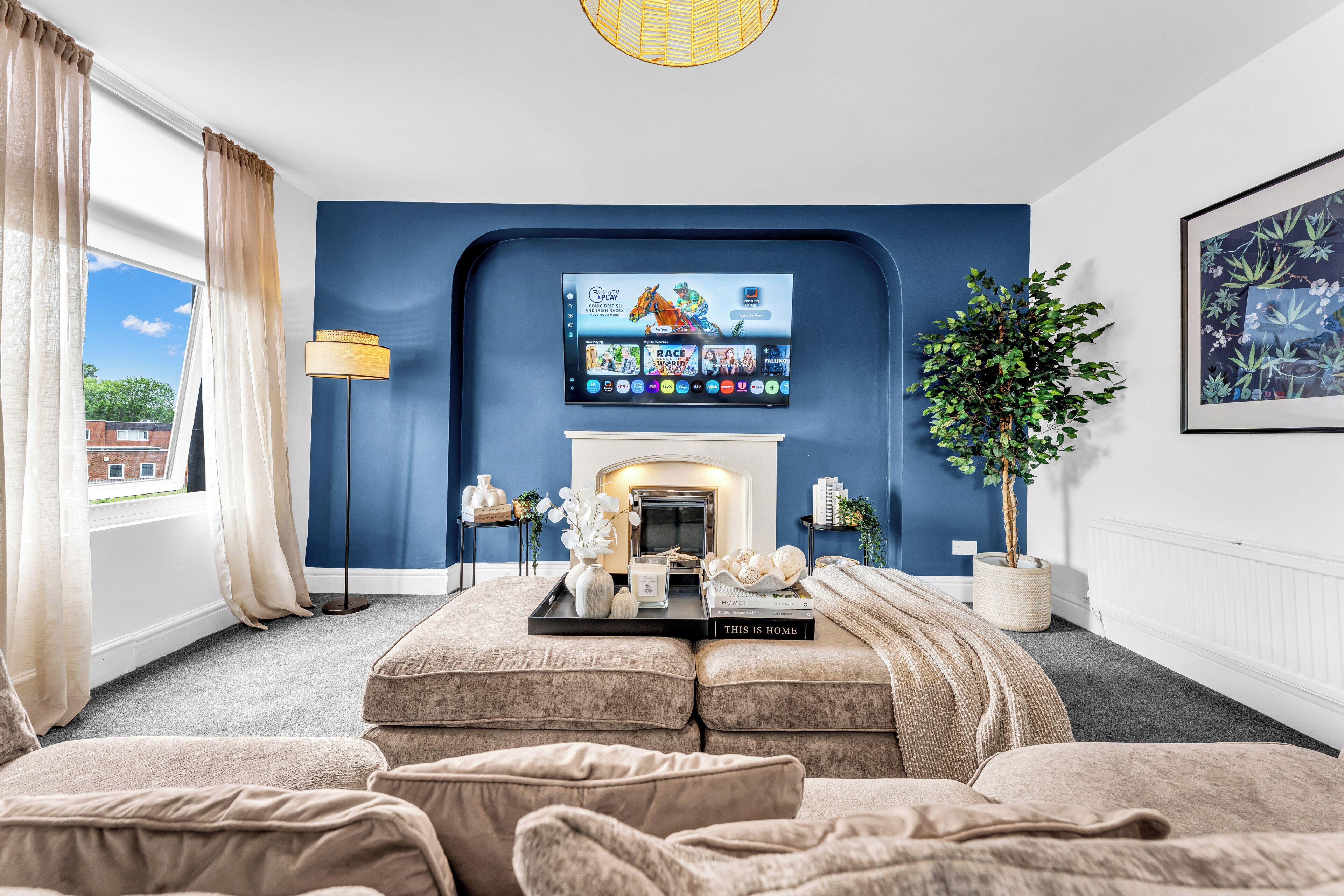 Una sala de estar con chimenea, televisor montado y un amplio ventanal con cortinas.
