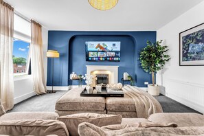 A living room with a fireplace, a mounted TV, and a large window with curtains.