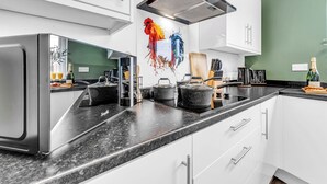 A modern kitchen with white cabinets, a black granite countertop, and a colorful rooster artwork on the wall.