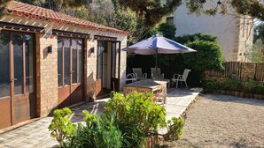 Ein Backsteinhaus mit großen Fenstern, einer Terrasse mit Tisch und Stühlen sowie einem Blumentopf.