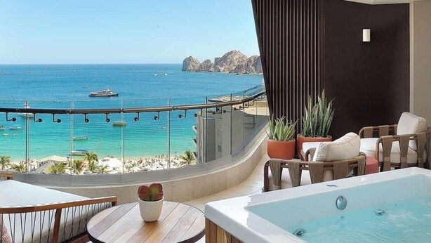 A balcony with a view of the sea, a hot tub, wicker furniture, and potted plants. - Two bedroom Corazon suite with hot tub, and ocean view (Cabo San Lucas)