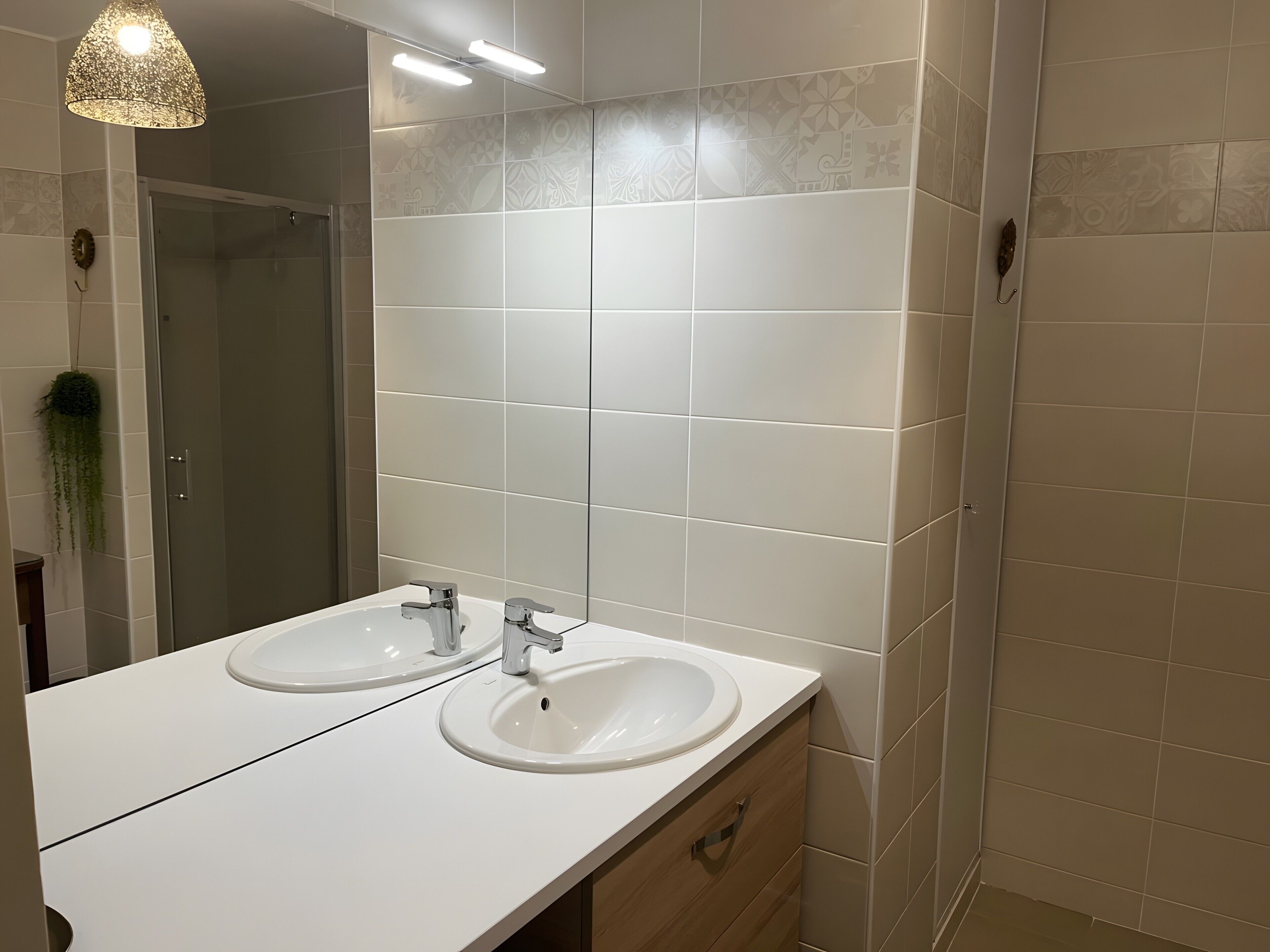 A bathroom with two sinks, a mirror, and a hanging light fixture.