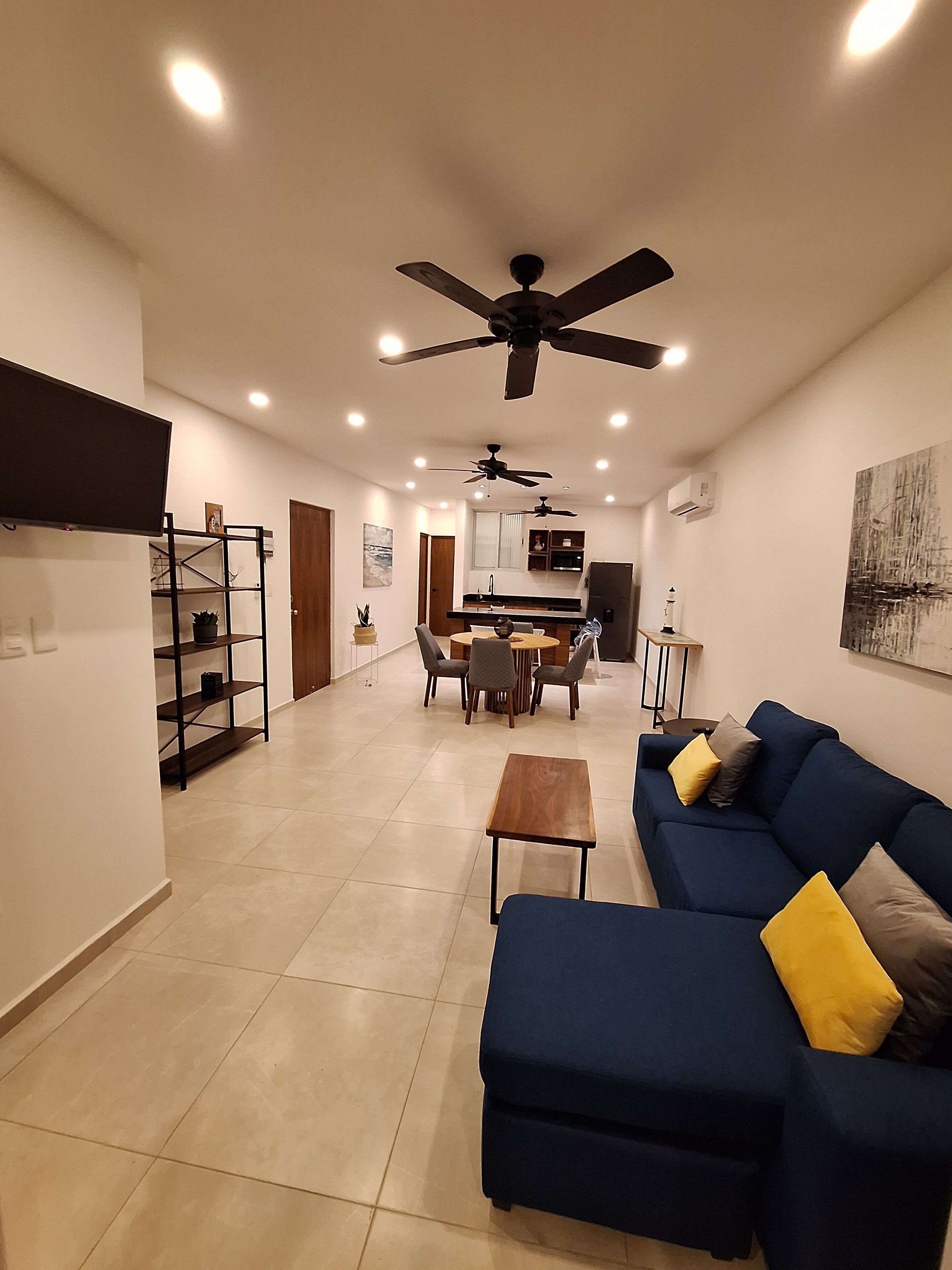 A modern living room with a blue sofa, a coffee table, and a dining area with chairs and a table.