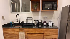 A modern kitchen with a black countertop, wooden cabinets, a built-in microwave, a coffee maker, a toaster, and a refrigerator. - 1. BEAUTIFUL APARTMENT JUST A FEW STEPS FROM THE BEACH (Progreso)