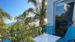 Een balkon met twee blauwe stoelen, een kleine tafel en een glazen deur naar een binnenruimte.