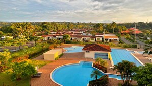 Een resort met een groot zwembad, meerdere gebouwen met rode daken en weelderige begroeiing.