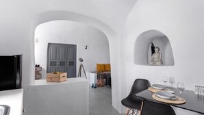 A modern interior with white walls, an arched doorway, a dining table with plates and glasses, and a Buddha statue. - Noelia Suites - Cave by ΜΡS (OIA)