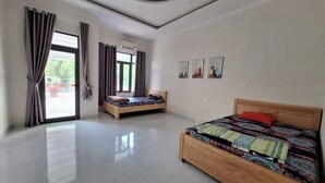 Une chambre spacieuse avec deux lits en bois, une grande fenêtre avec des rideaux et un plafond doté d’un éclairage encastré.