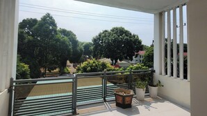 Un balcon doté d’une rambarde en métal, d’un sol carrelé et offrant une vue sur les arbres et les bâtiments.
