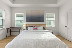 Ein Schlafzimmer mit Bett, Nachttisch, Lampe und einem Kunstwerk an der Wand.