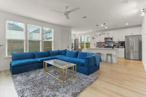 Ein modernes Wohnzimmer mit einer Eckcouch, einem Glastisch und einer Küchenzeile mit Edelstahlgeräten.