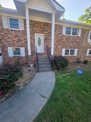 A two-story brick building with a front entrance, a small porch, and a front yard with a sidewalk leading to the entrance.