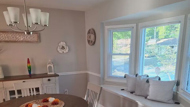 A dining area with a round table, chairs, a chandelier, a window seat with pillows, and a decorative wall piece. - Fabulous 3-bedroom house with AC in charming Jonesboro (Jonesboro)