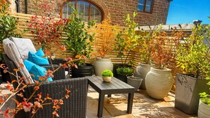 Eine Terrasse mit Korbmöbeln, Topfpflanzen und Steinboden.