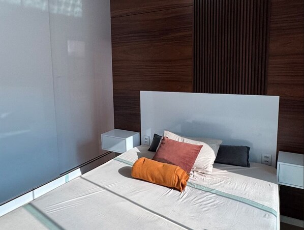 A modern bedroom with a large bed, two bedside tables, and a view of the outside.