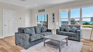 Een moderne woonkamer met twee grijze banken, een salontafel en grote ramen met uitzicht op zee.