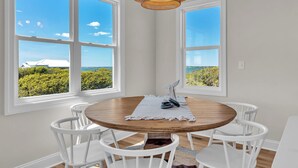 Een eetruimte met een ronde tafel, witte stoelen en uitzicht door grote ramen.