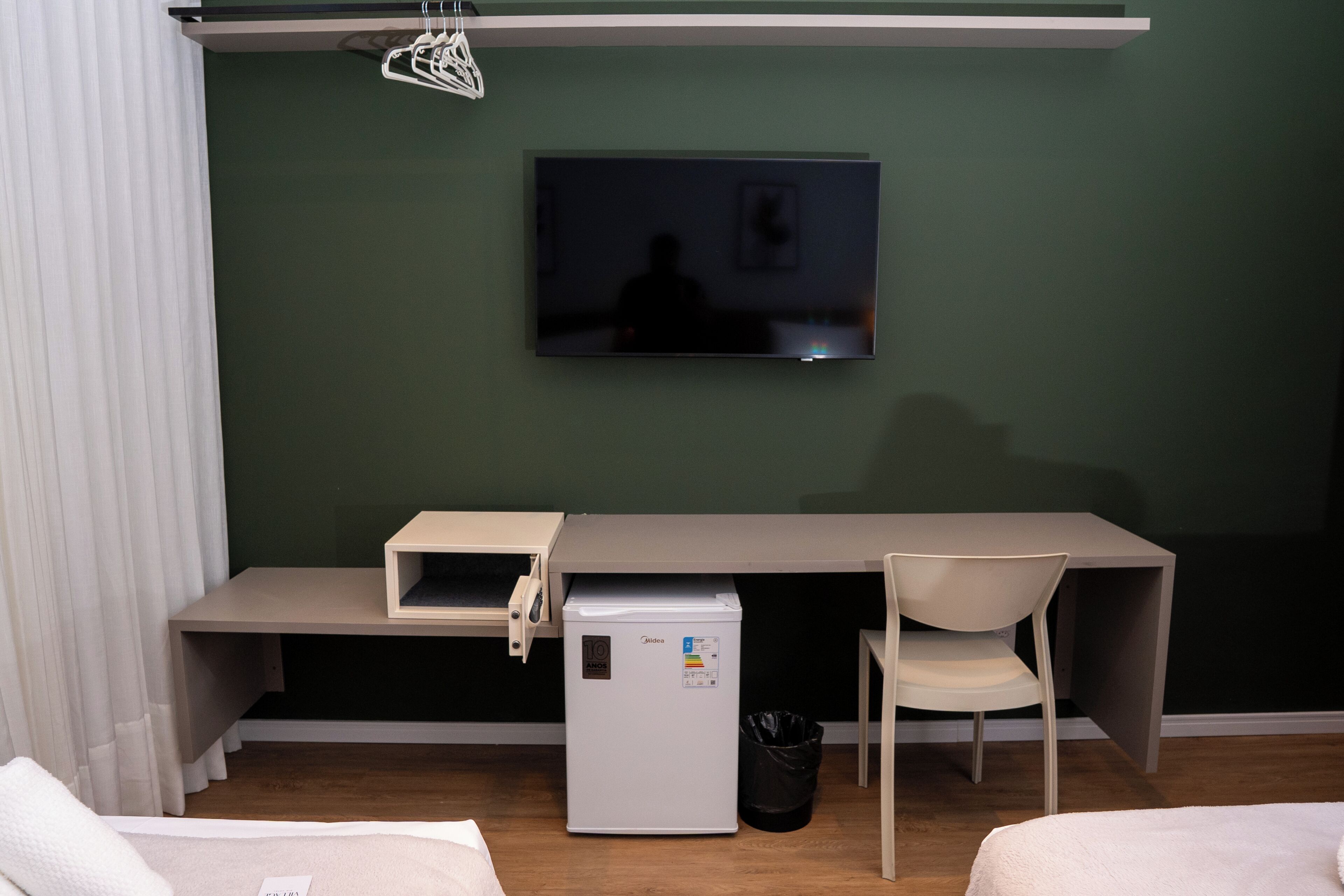 Een kleine kamer met een bed, een bureau met stoel, een televisie, een kleine koelkast en een afvalbak.