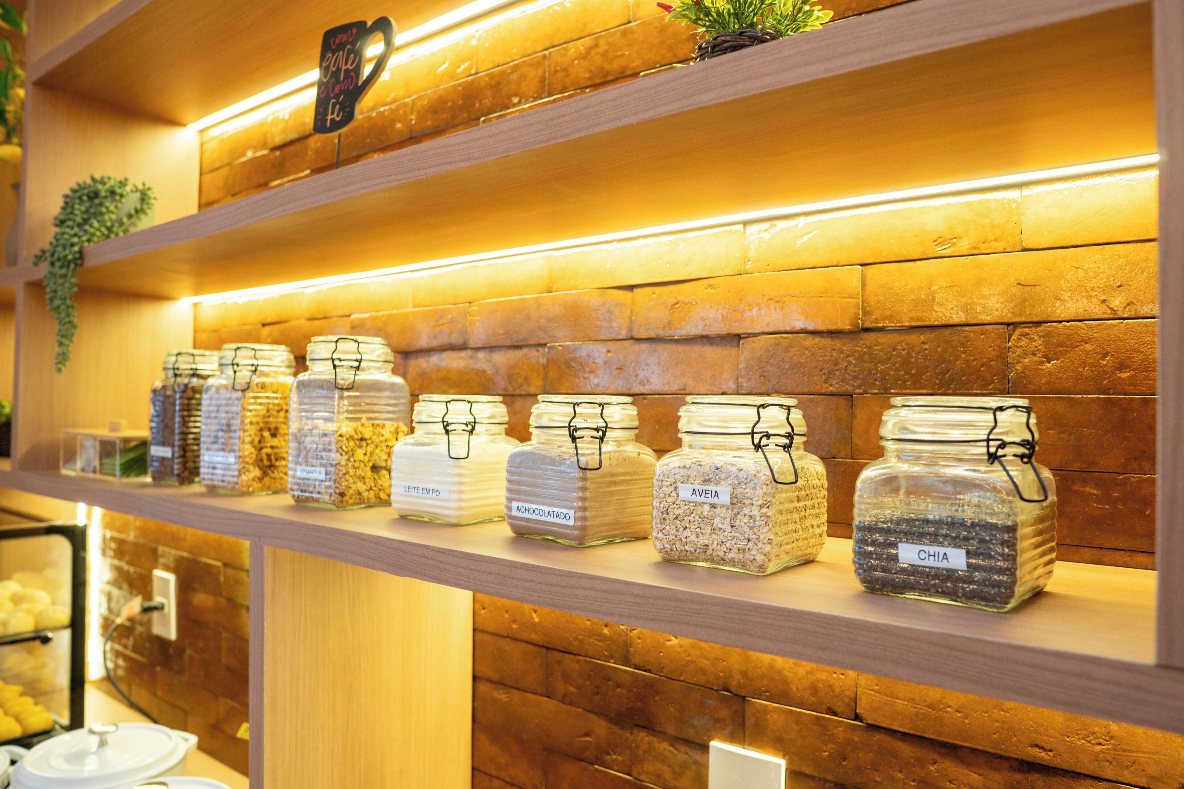A shelf with labeled jars of food items, a sign above indicating a cafe, and a brick wall background.