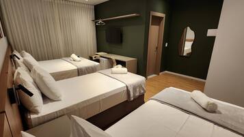 A hotel room with two beds, a TV, a mirror, and a wooden floor.