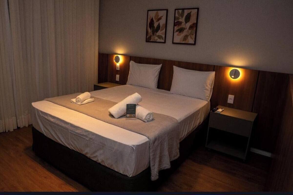 Une chambre d’hôtel avec un grand lit, deux tables de chevet, une petite table et une lampe fixée au mur.