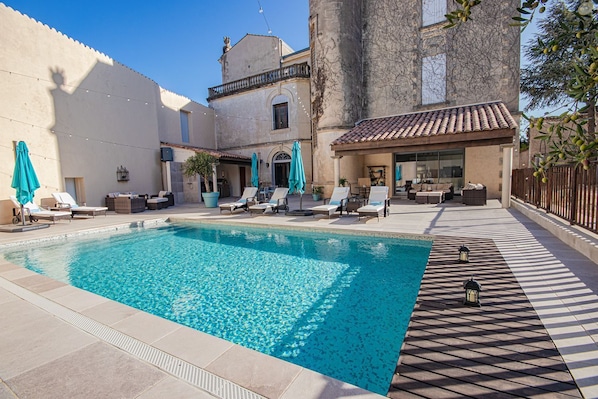 A swimming pool with lounge chairs and umbrellas, a tiled deck, and a building with a tiled roof.