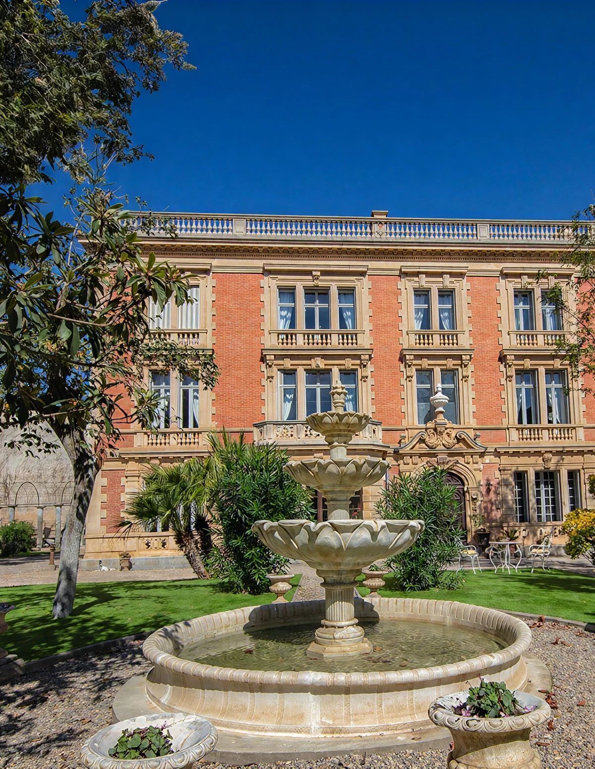 A historic building with a central fountain, surrounded by a well-maintained garden.
