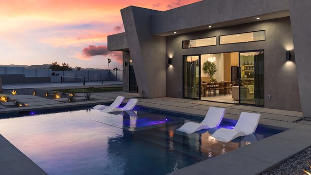 Een modern huis met een zwembad, lounge stoelen en een terras.