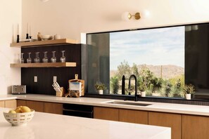 A modern kitchen with a large window, wooden cabinets, a built-in wine rack, and a bowl of lemons. - Villa Solara│Pool Pickleball Sauna Stargazing dome (Joshua Tree)