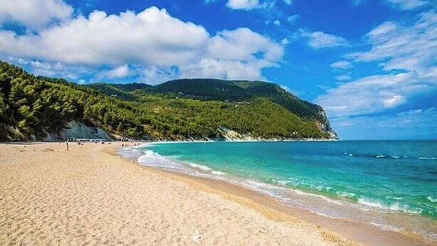 A beach with clear turquoise water, sandy shore, and a forested hill in the background. - Piccolo Resort sul Conero – Relax con Vista Mare tra Natura e Silenzio (Marche)