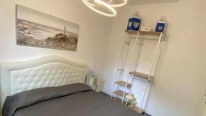 A bedroom with a bed, a white headboard, a pendant light, a shelf with items, and a painting on the wall. - Piccolo Resort sul Conero – Relax con Vista Mare tra Natura e Silenzio (Marche)