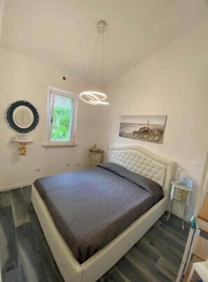A bedroom with a bed, a window, a wall-mounted mirror, a picture, and a ceiling light fixture. - Piccolo Resort sul Conero – Relax con Vista Mare tra Natura e Silenzio (Marche)