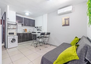 A compact room with a bed, a washing machine, a dining table with chairs, a kitchen area, and an air conditioning unit. - Central apartment close to everything with swimming pool and parking. (San Bartolomé de Tirajana)
