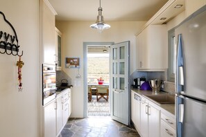 A narrow kitchen with a stone floor, a hanging light fixture, and a view into a dining area. - Villa Kea Royale - Two Bedroom Villa, Sleeps 5 (Kastriani)