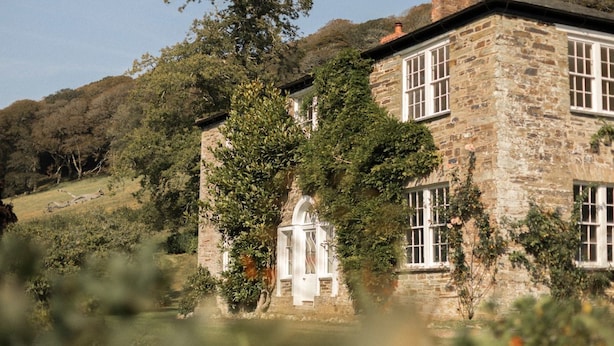 A stone building with a central arched doorway, surrounded by greenery and hills.