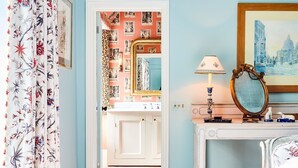 A room with a door leading to a bathroom with a mirror and a framed picture on the wall.