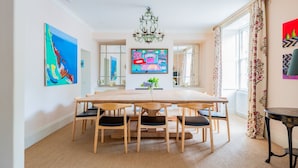A dining area with a large wooden table, six chairs, a chandelier, and artwork on the walls.