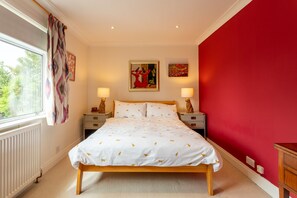 Une chambre avec un grand lit, deux tables de chevet, une fenêtre avec des rideaux et un mur rouge.