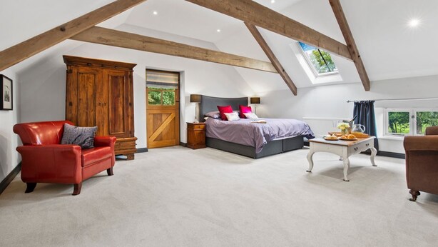 A bedroom with a sloped ceiling, a bed, a red leather chair, a wooden wardrobe, and a window with a view. - Welsh Coach House - Five Bedroom Villa, Sleeps 9 (Tan-y-groes)