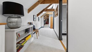 A hallway with a white console table, a lamp, and a chair. There are bookshelves with books and a door at the end. - Welsh Coach House - Five Bedroom Villa, Sleeps 9 (Tan-y-groes)
