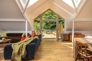 An interior with a high ceiling, a sofa, a dining table, and a view of the outdoors.