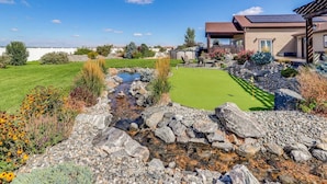Propiedad residencial con jardín trasero que incluye un campo de golfito, un pequeño arroyo y un patio amoblado.