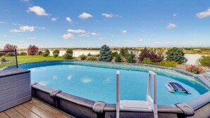 Una piscina con cubierta de madera, rodeada de vegetación y un cielo despejado.