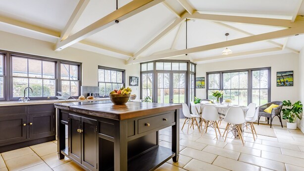 A kitchen with a central island, large windows, and a dining area with chairs and a table. - Sandon Manor - Seven Bedroom Villa, Sleeps 16 (Sandon)